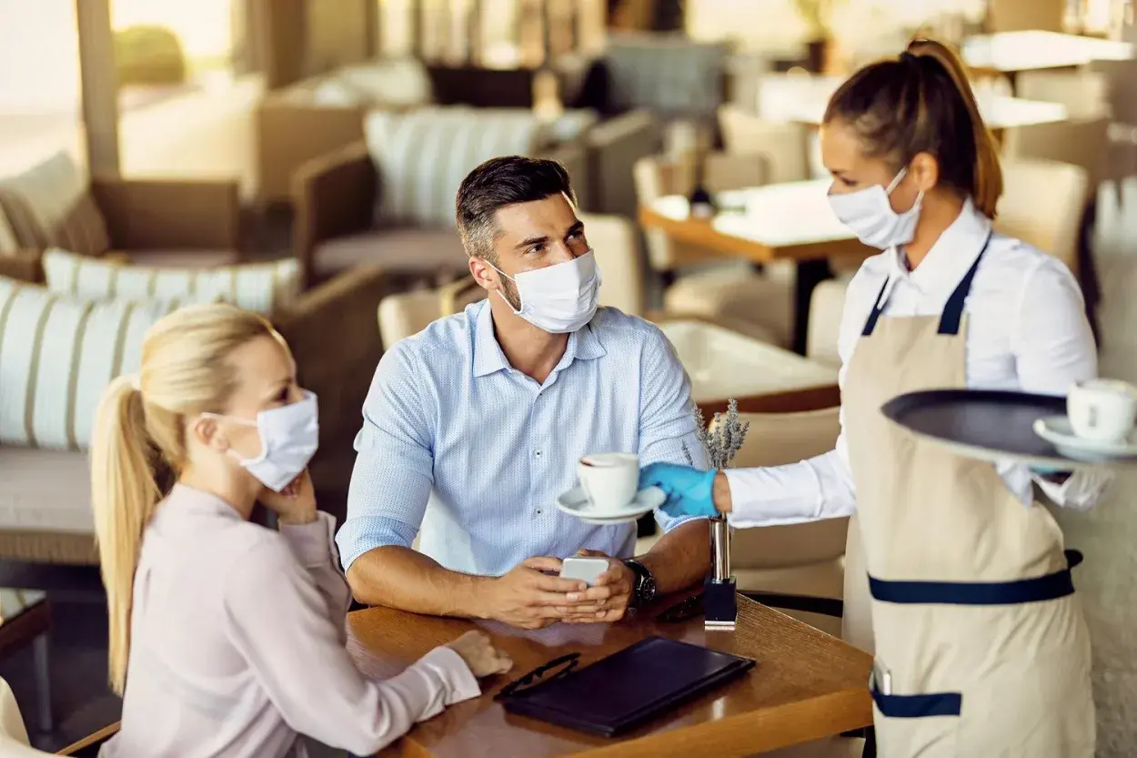 a waitress serving a cup of coffee to a couple in the cafe during covid19 pandemic